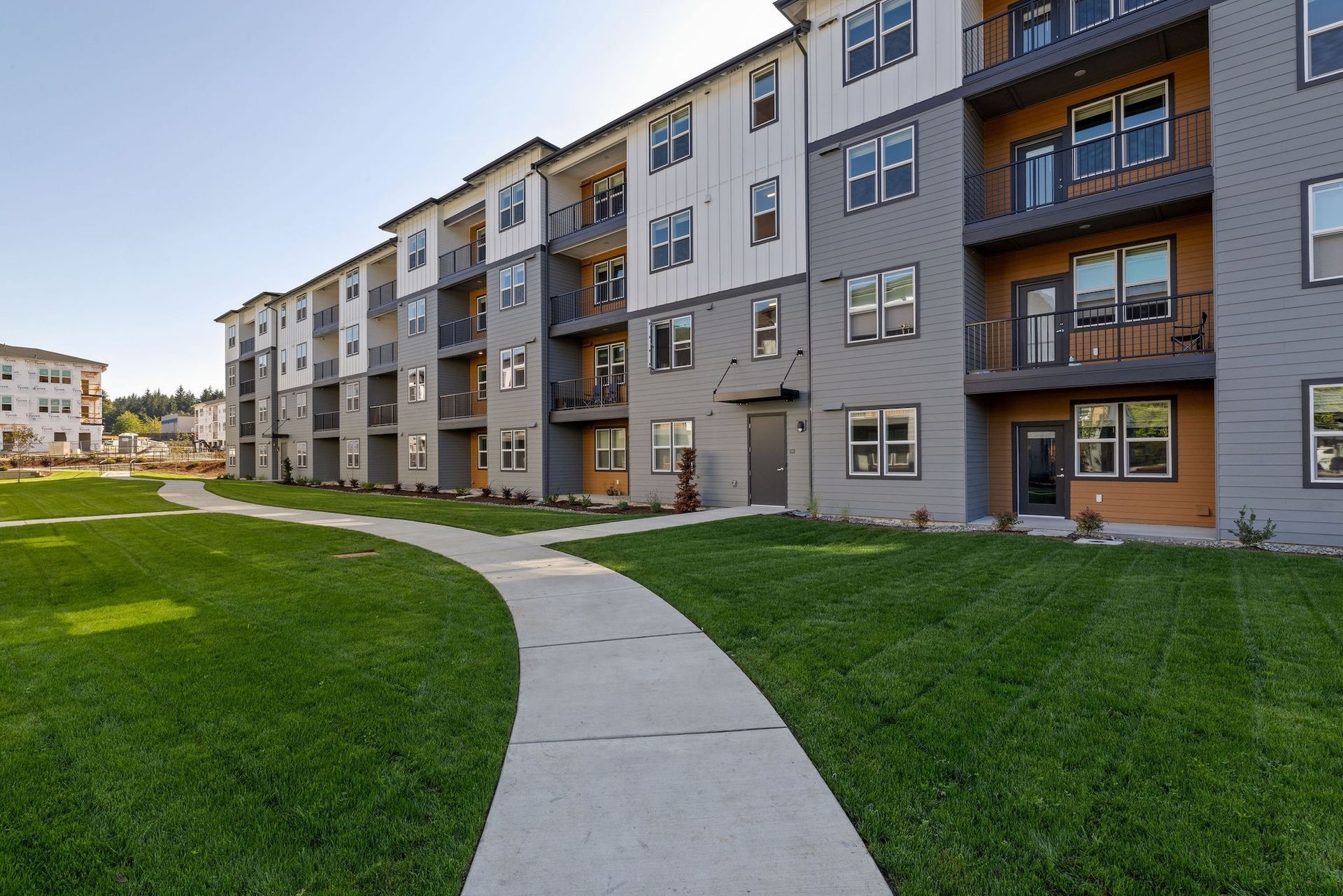 Modern apartment buildings beside a curved concrete walkway and green lawn