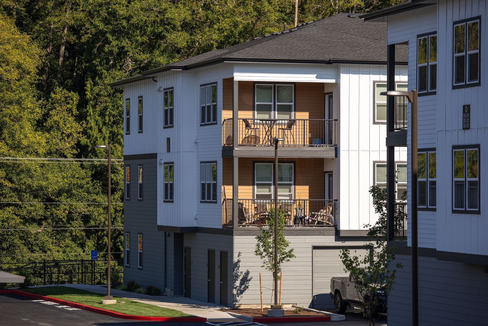 Modern apartment building with balconies and white-and-gray siding beside trees