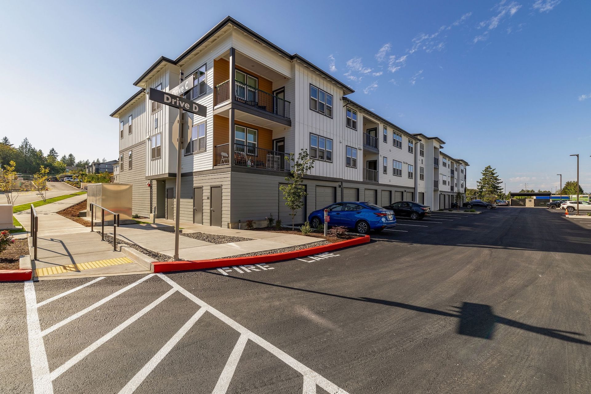 Modern apartment building with parked cars and a paved parking lot under a clear blue sky