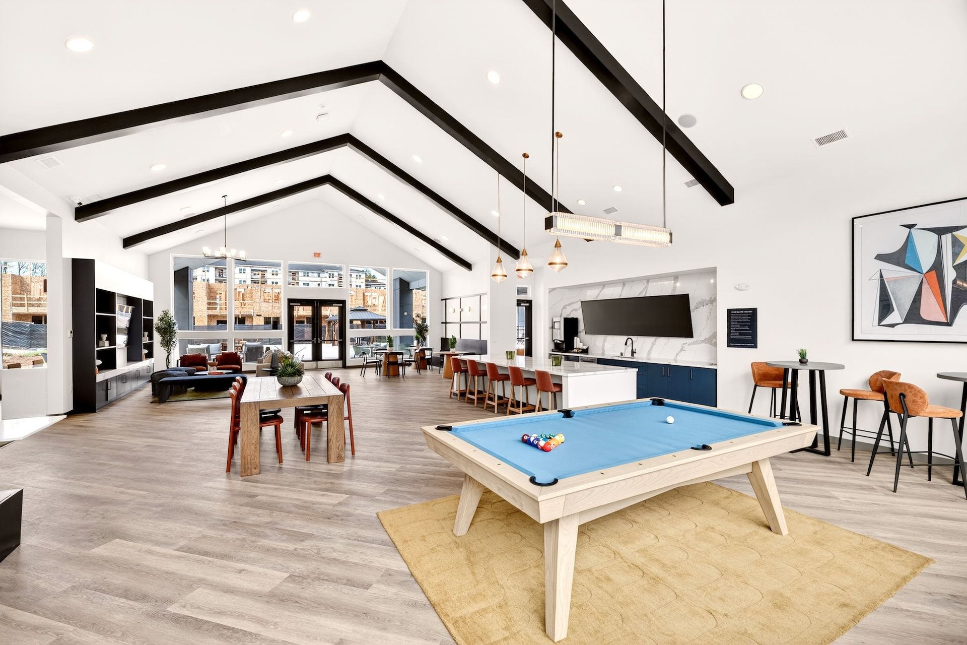 Bright modern lounge with pool table, wooden tables, high ceilings, and large windows