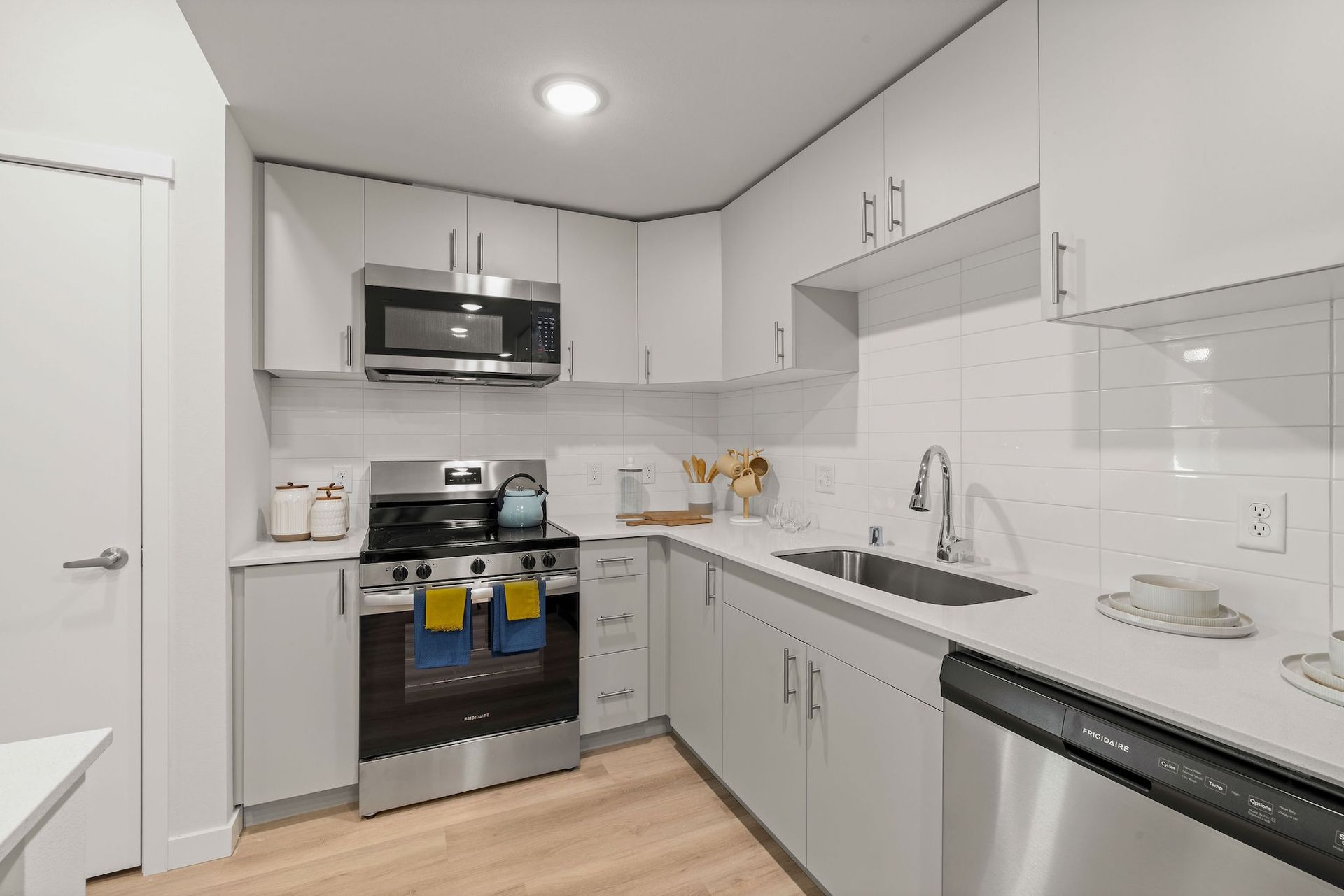 Modern white kitchen with stainless steel appliances, black countertops, and light wood flooring