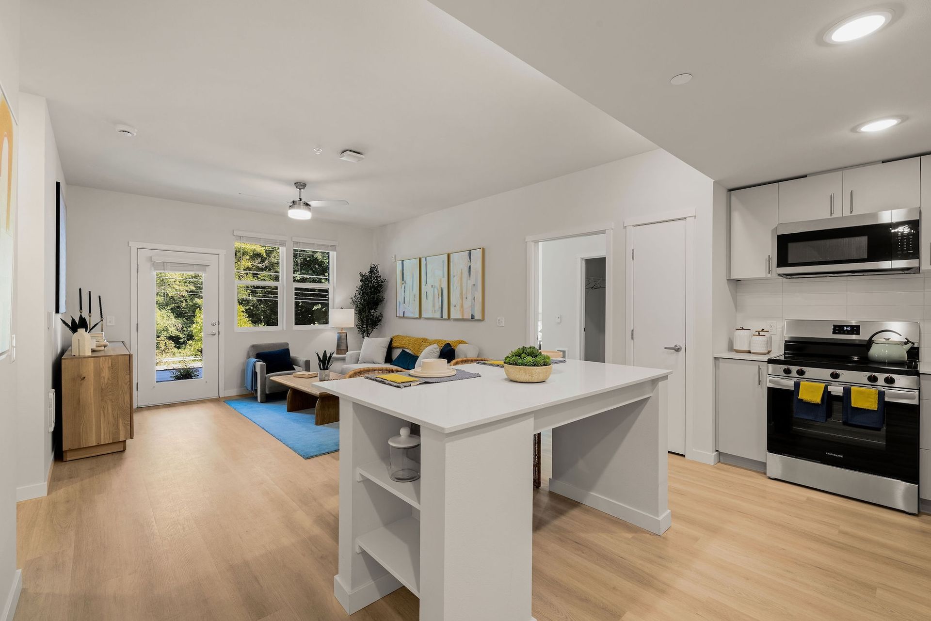 Bright open kitchen and living room with white cabinets, wood floors, island, and blue sofa by large windows