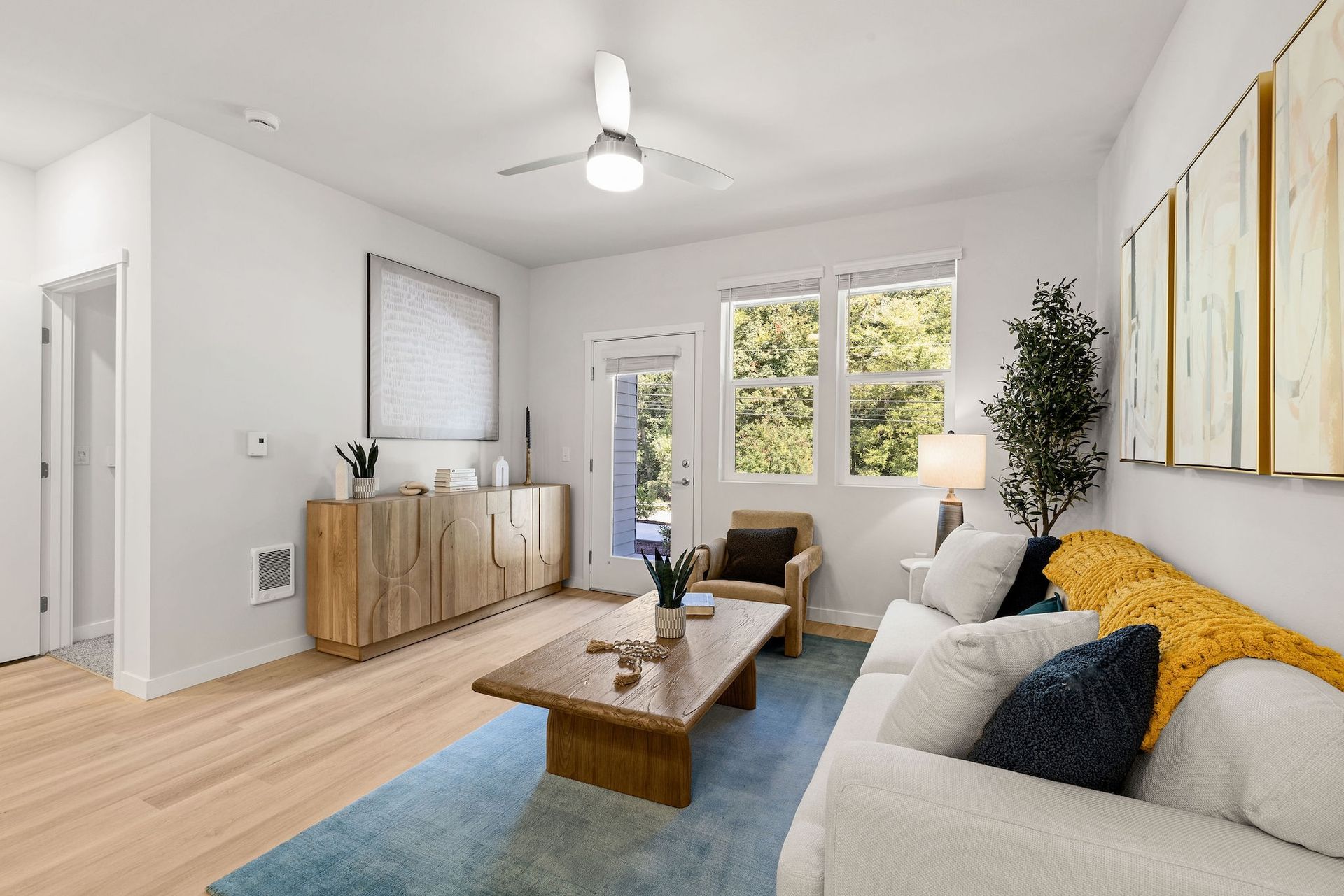 Bright modern living room with gray sofa, wood coffee table, blue rug, and large windows.