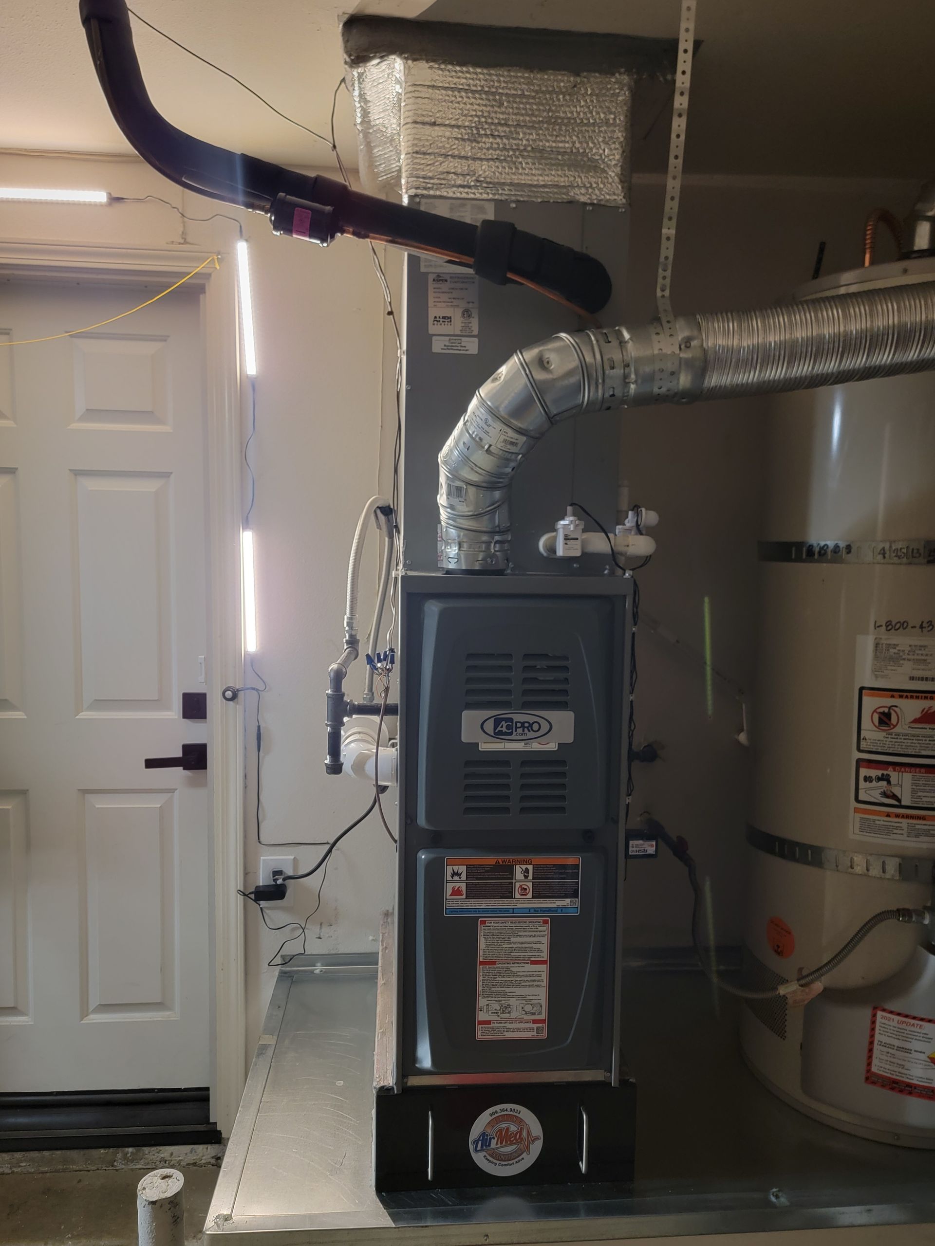 A furnace is sitting in a garage next to a water heater.