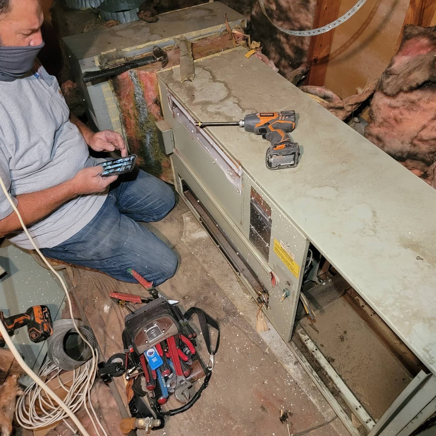 A man wearing a mask is working on an air conditioner