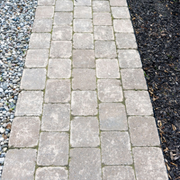 A stone paver walkway with light gray bricks bordered by gravel and dark mulch