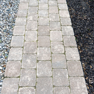 A stone paver walkway with light gray bricks bordered by gravel and dark mulch