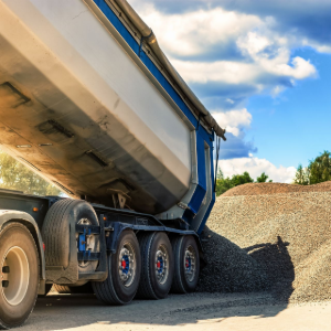 Dump truck unloading gravel beside a large gravel pile under a blue sky