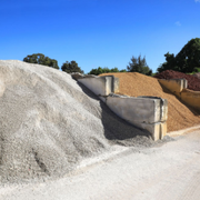 Piles of gravel, sand, and stone stacked outdoors under a clear blue sky.