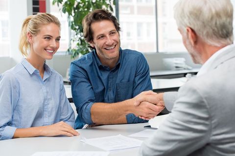 Two people meeting with an older man in a bright office, shaking hands over a table