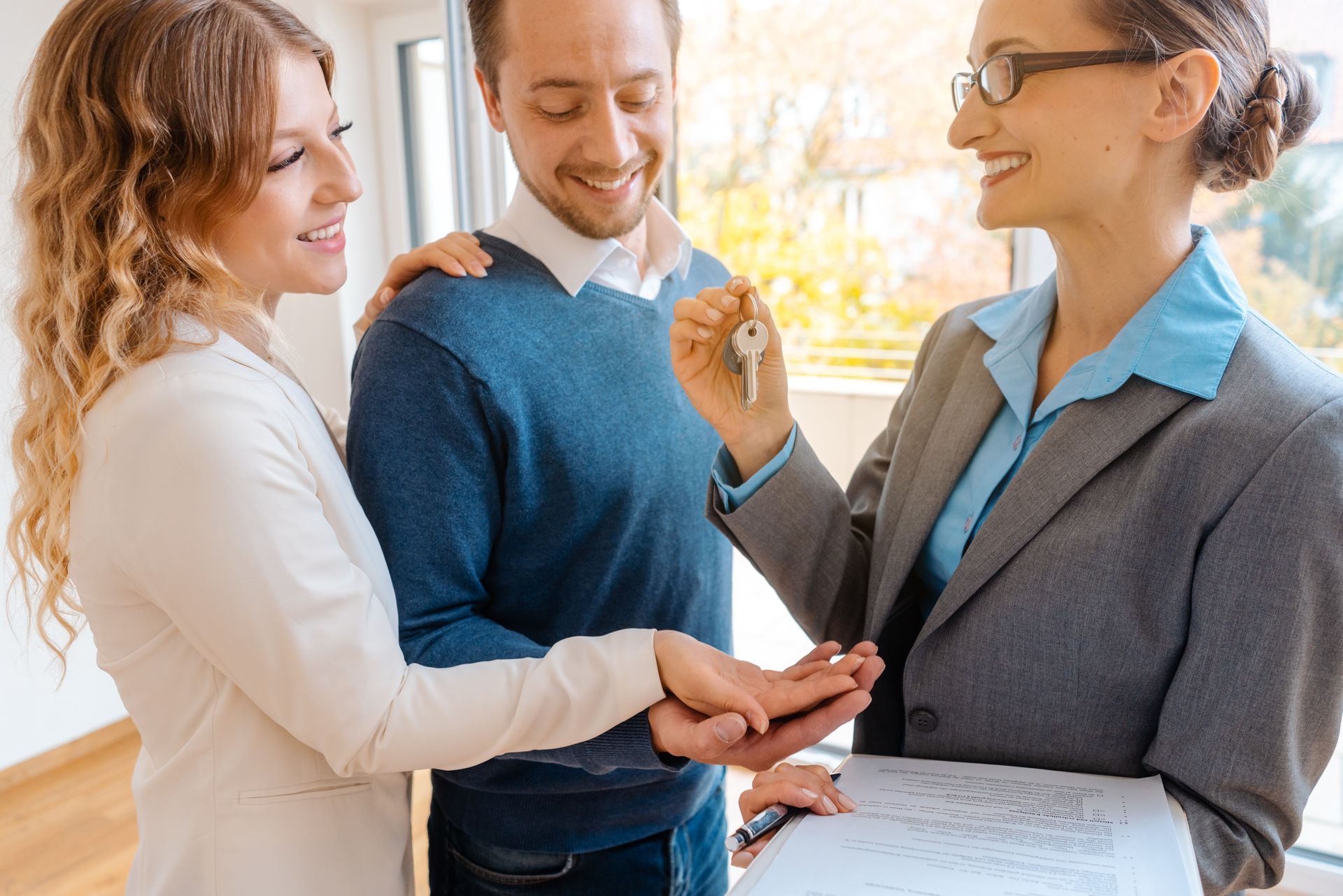 Three coworkers smiling and shaking hands in a bright office with a clipboard nearby