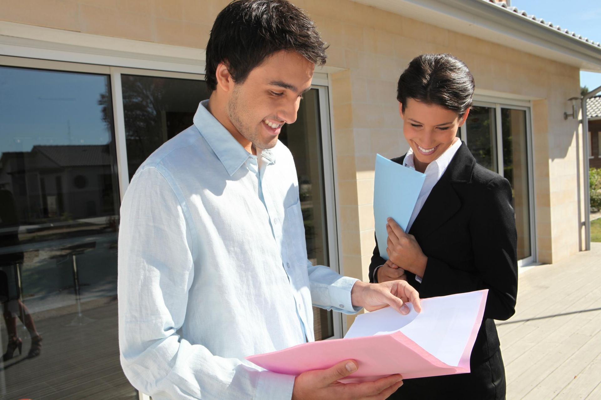 Two men reviewing paperwork outside a building, one holding a pink folder
