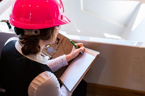 Person in a pink hard hat writing on a clipboard near a bright window