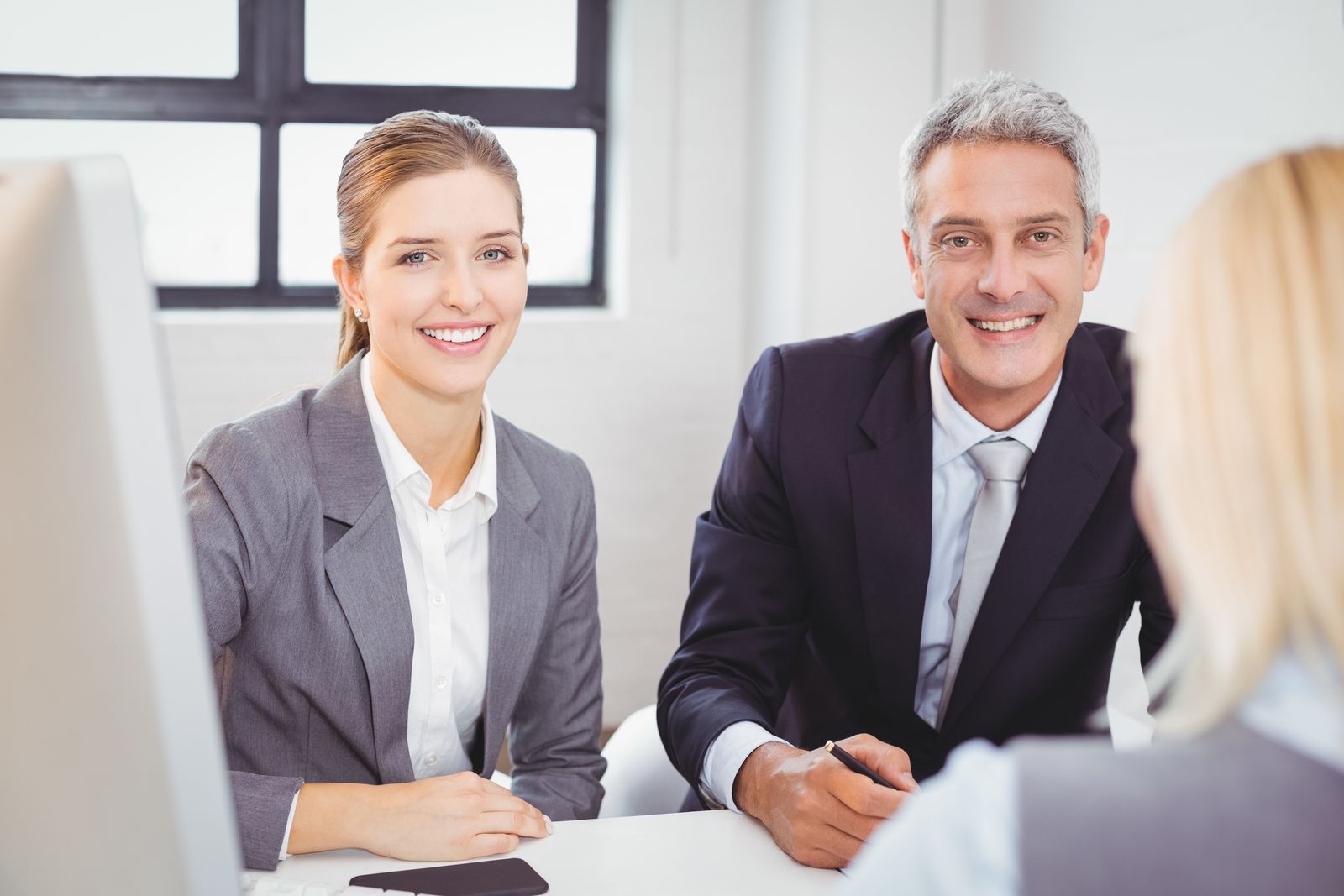 Two business professionals smiling across a desk in a bright office during a meeting