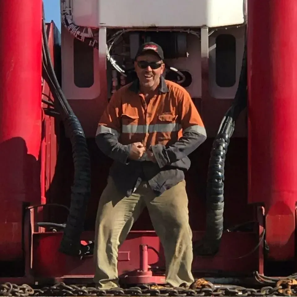 Man Flexing Biceps in Work Clothes, Standing Against Red Equipment — Boland Contracting In Wellington, NSW