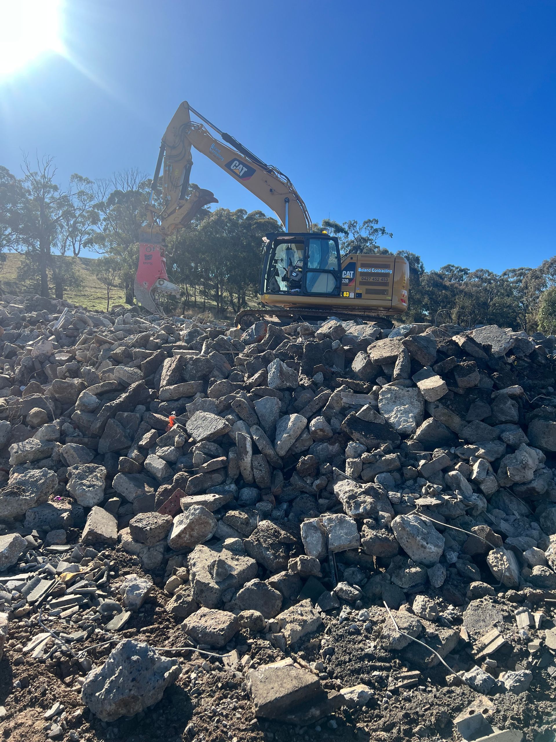 Excavator on a Pile of Rubble Under a Bright Sky — Boland Contracting In Wellington, NSW