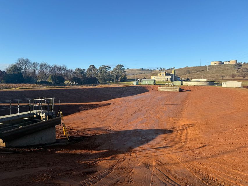 A Dry Reddish-Brown Sediment Pond With Industrial Structures — Boland Contracting In Wellington, NSW