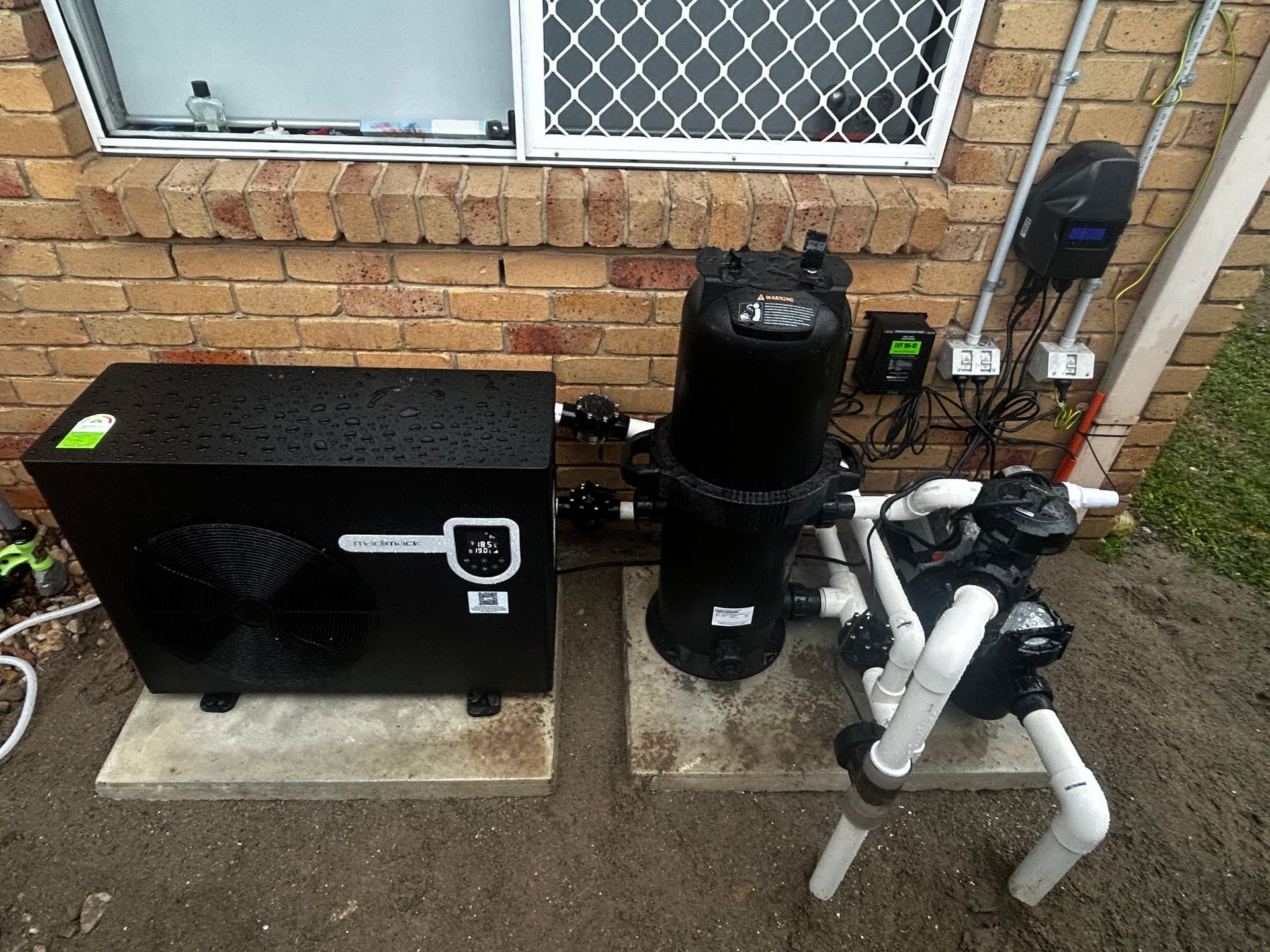Black Outdoor Hvac and Filtration Equipment Beside a Brick House Wall — Bromage Pool Heating in Kawana, QLD