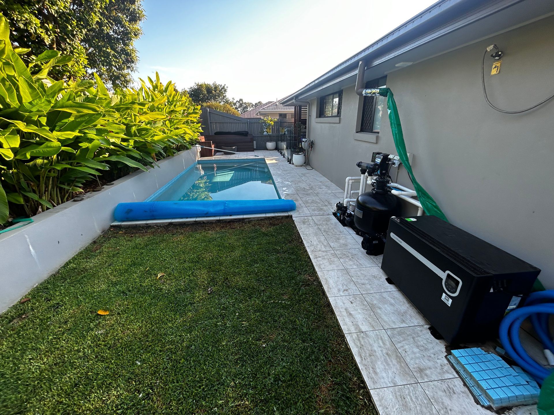 Backyard Pool With Blue Cover, Grass Lawn, and Patio Beside a House — Bromage Pool Heating in Maleny, QLD