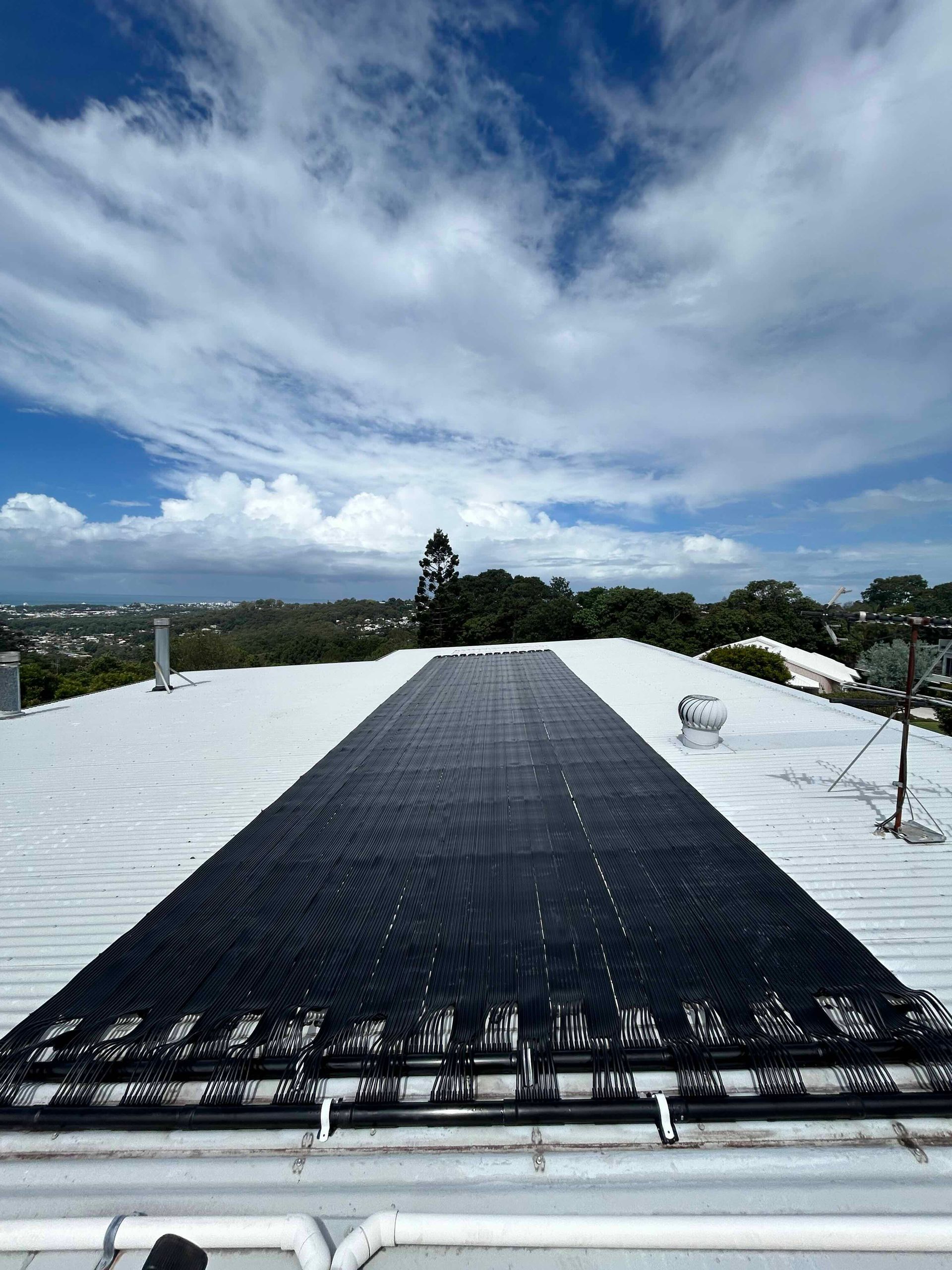 Black Roof Tarp on a White Rooftop With a Cloudy Sky and Distant Landscape View — Bromage Pool Heating in Maroochydore, QLD