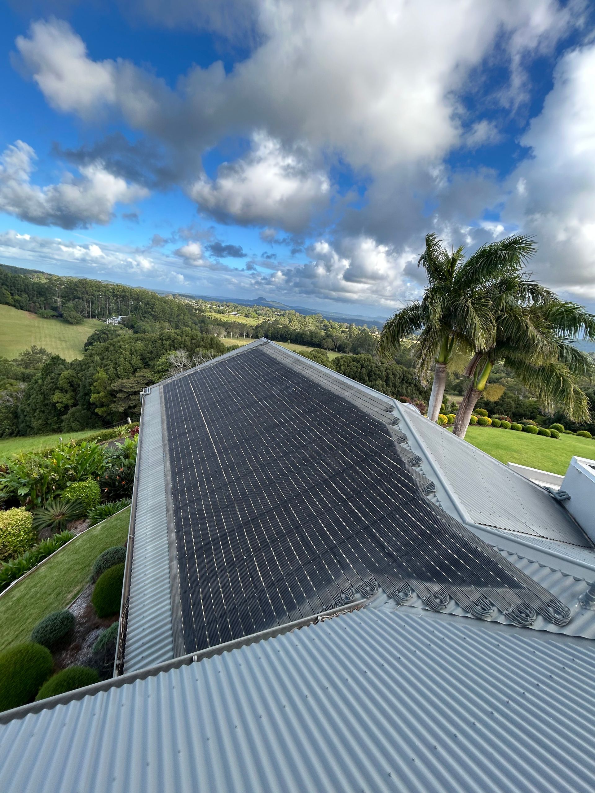 Rooftop With Dark Shingles Overlooking Green Hills, Palm Trees, and a Cloudy Blue Sky — Bromage Pool Heating in Maleny, QLD