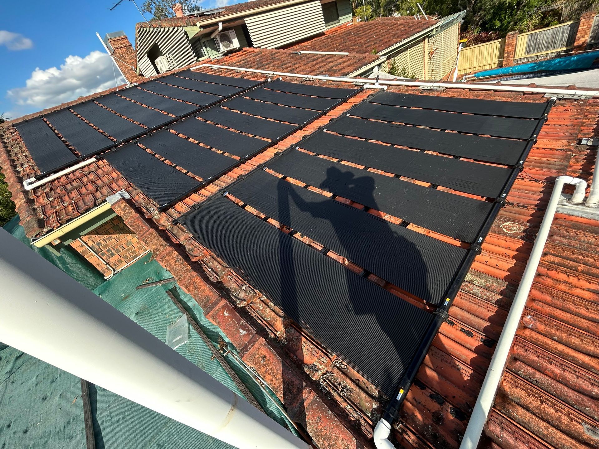Roof Covered With Black Solar Panels on a Red-tiled House Under a Blue Sky — Bromage Pool Heating in Kawana, QLD