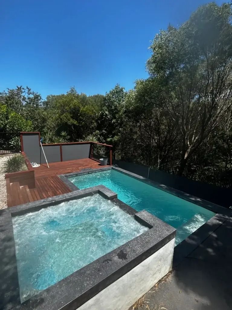 Modern backyard pool with a raised spa, turquoise water, wood deck, and trees under a clear blue sky — Bromage Pool Heating in Maroochydore, QLD