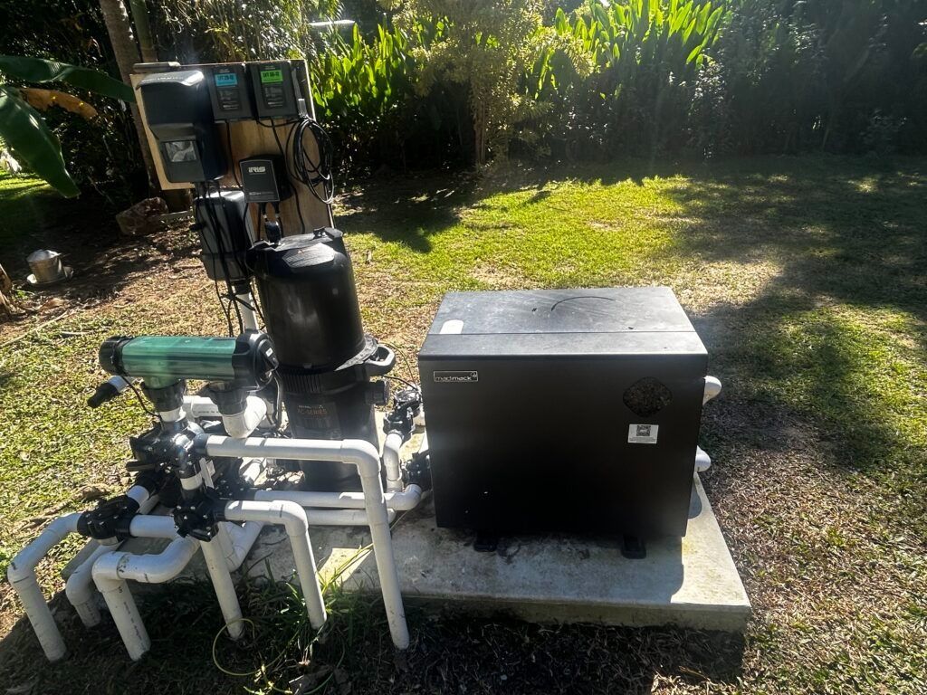 Outdoor Equipment Setup With a Black Metal Box on a Concrete Slab Beside a White Chair and Small Device on a Sunny Lawn — Bromage Pool Heating in Noosa, QLD