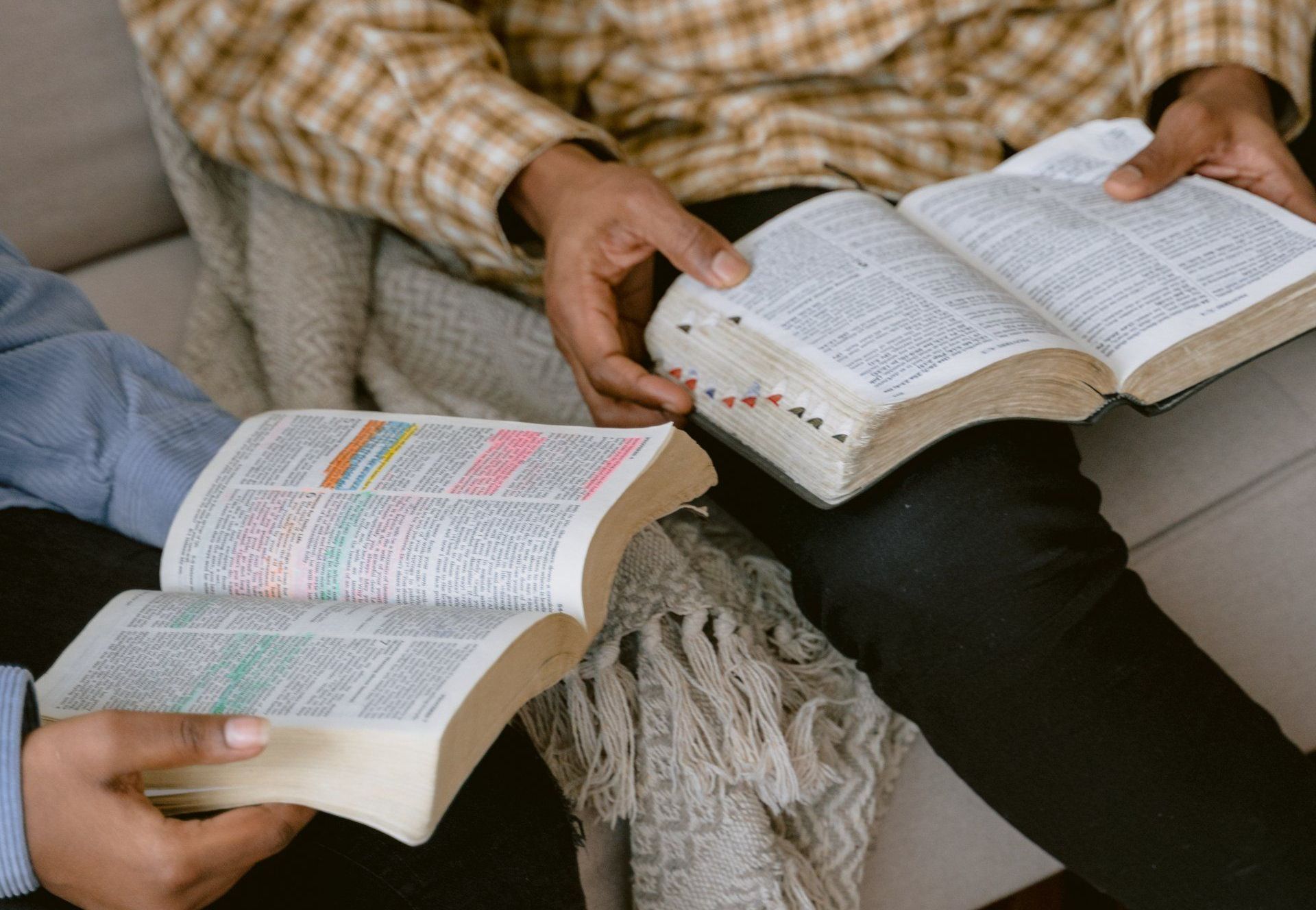 two people are sitting on a couch reading bibles .