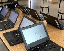 A row of laptops sitting on top of a wooden table.