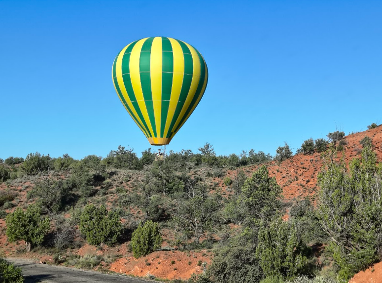  A hot air balloon with a green and yellow vertical-striped balloon hovers above the Arizona desert.