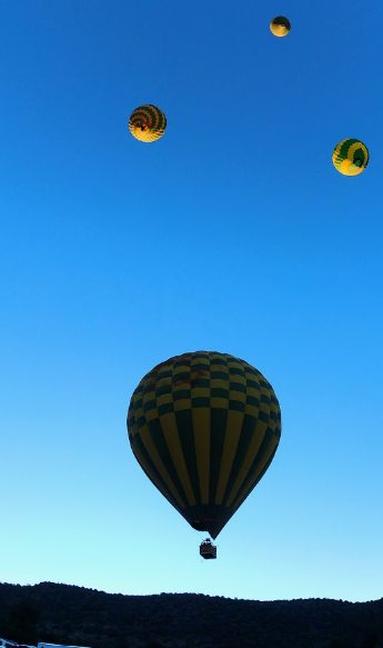 Four hot air balloons are floating in the sky at dusk. One is close, and three are further away.