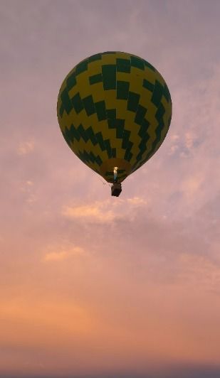 A green and white hot air balloon is floating in the sky. The sky is in different shades of purple a