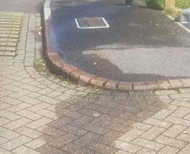 A car is parked on the side of the road next to a brick sidewalk.