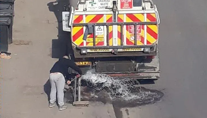 A man is standing next to a truck that is cleaning a hole in the road.