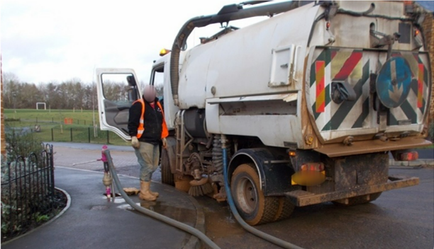 A man is standing next to a vacuum truck with a hose attached to it.