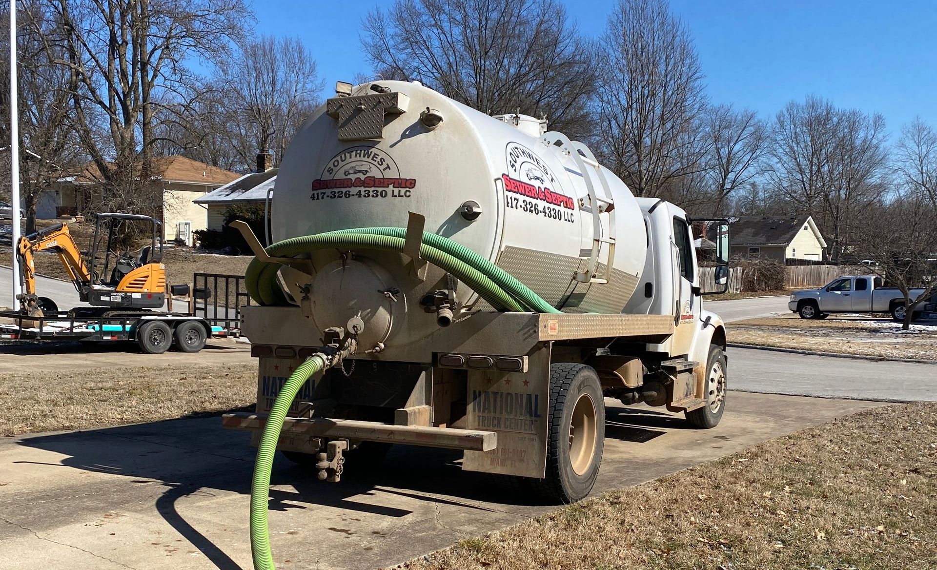 A vacuum truck with a green hose attached to it is parked on the side of the road.