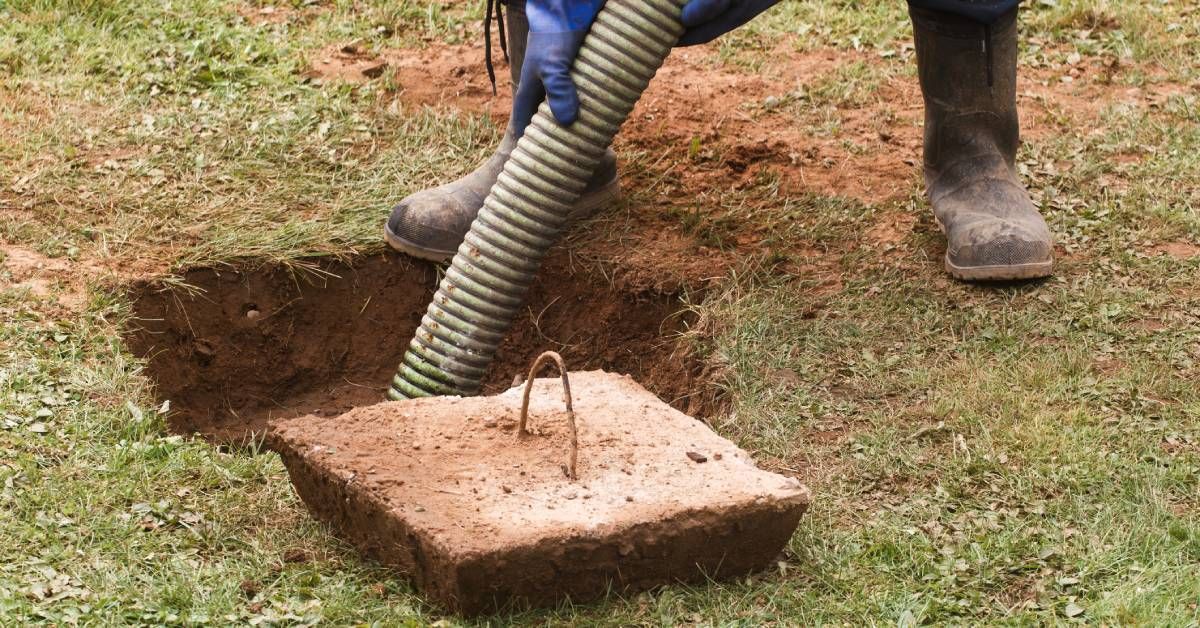 A worker wearing wearing heavy-duty rubber gloves and boots is pumping out an underground septic tan
