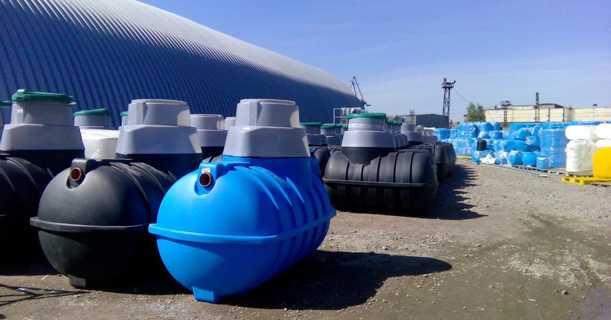 A row of septic tanks outside on a dirt surface. Most of the septic tanks are black with one septic