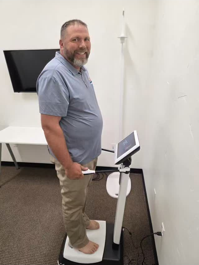 A person standing barefoot on a bioimpedance analysis scale while holding the device's handles in an office setting.