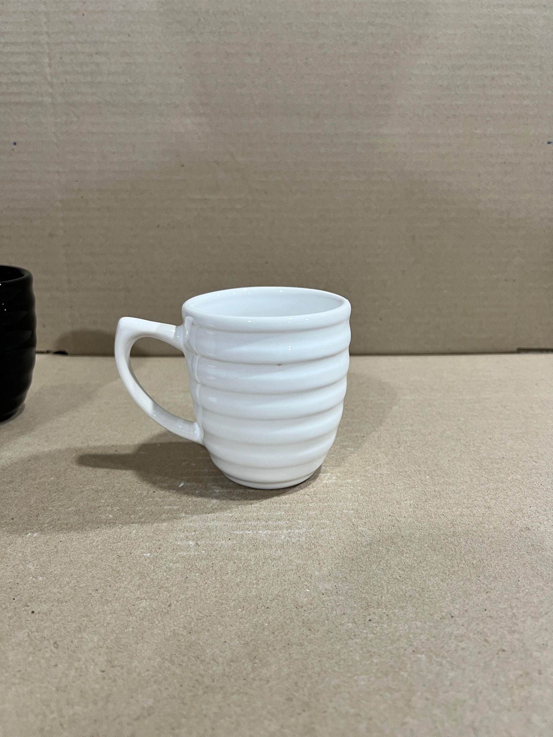 Taza de cerámica blanca con diseño acanalado, apoyada sobre una superficie de color marrón claro.