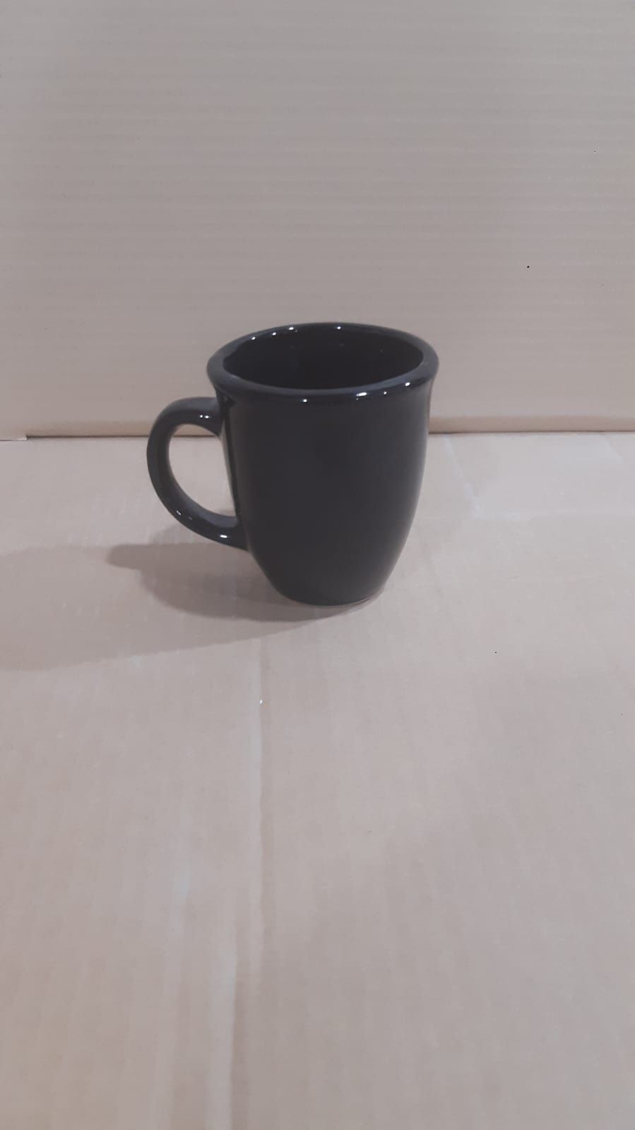Taza de café negra con forma redondeada sobre una superficie clara.