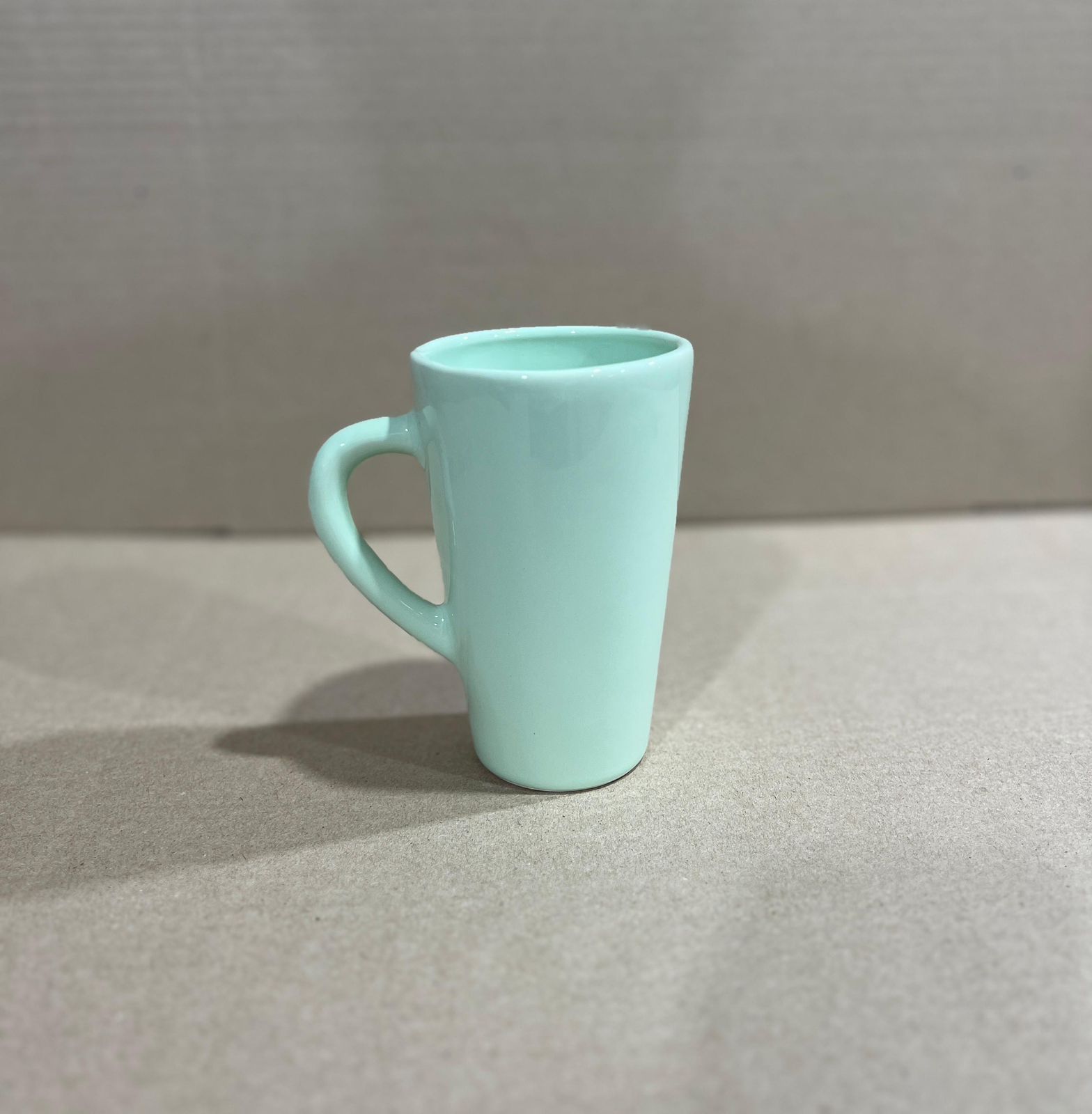 Taza de cerámica de color verde menta con asa curvada, colocada sobre una superficie de color claro.