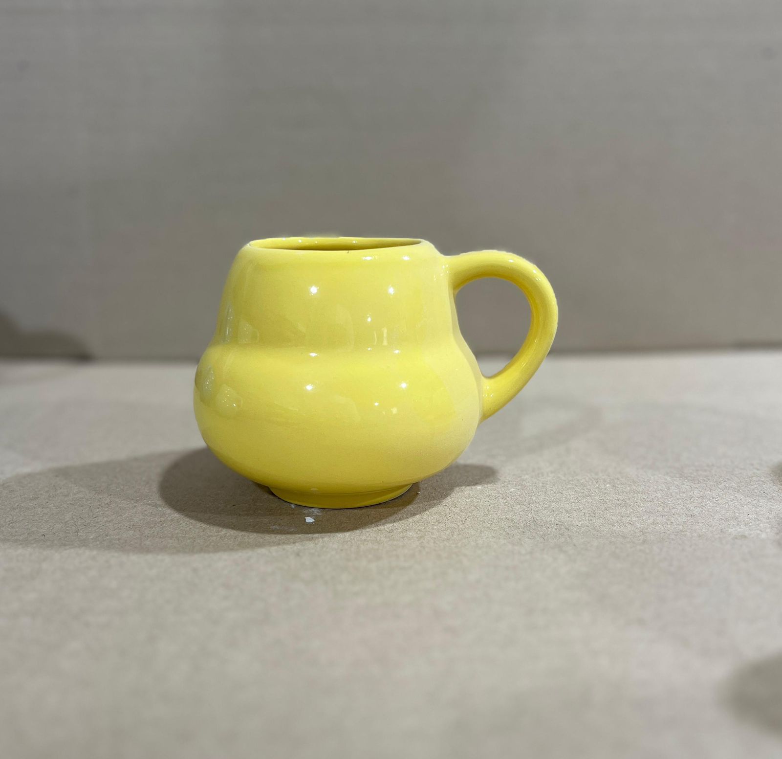 Taza de cerámica de color amarillo con cuerpo y asa redondos, sobre superficie gris claro.
