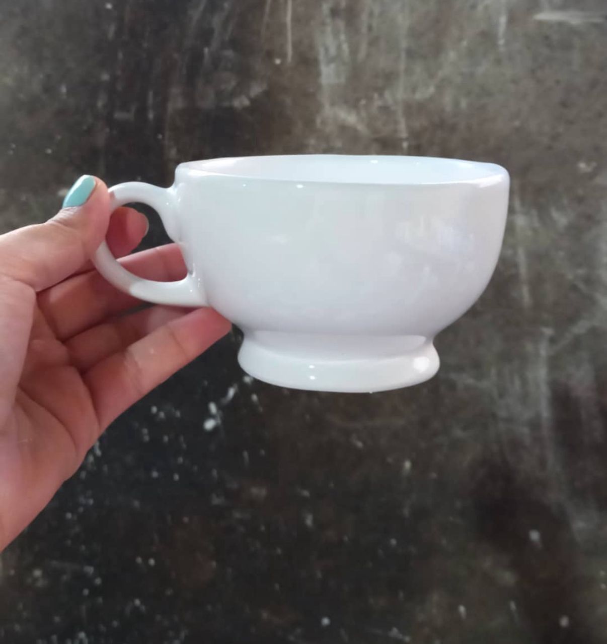 Mano sosteniendo una pequeña taza de té blanca con un cuenco y un asa redondeados.