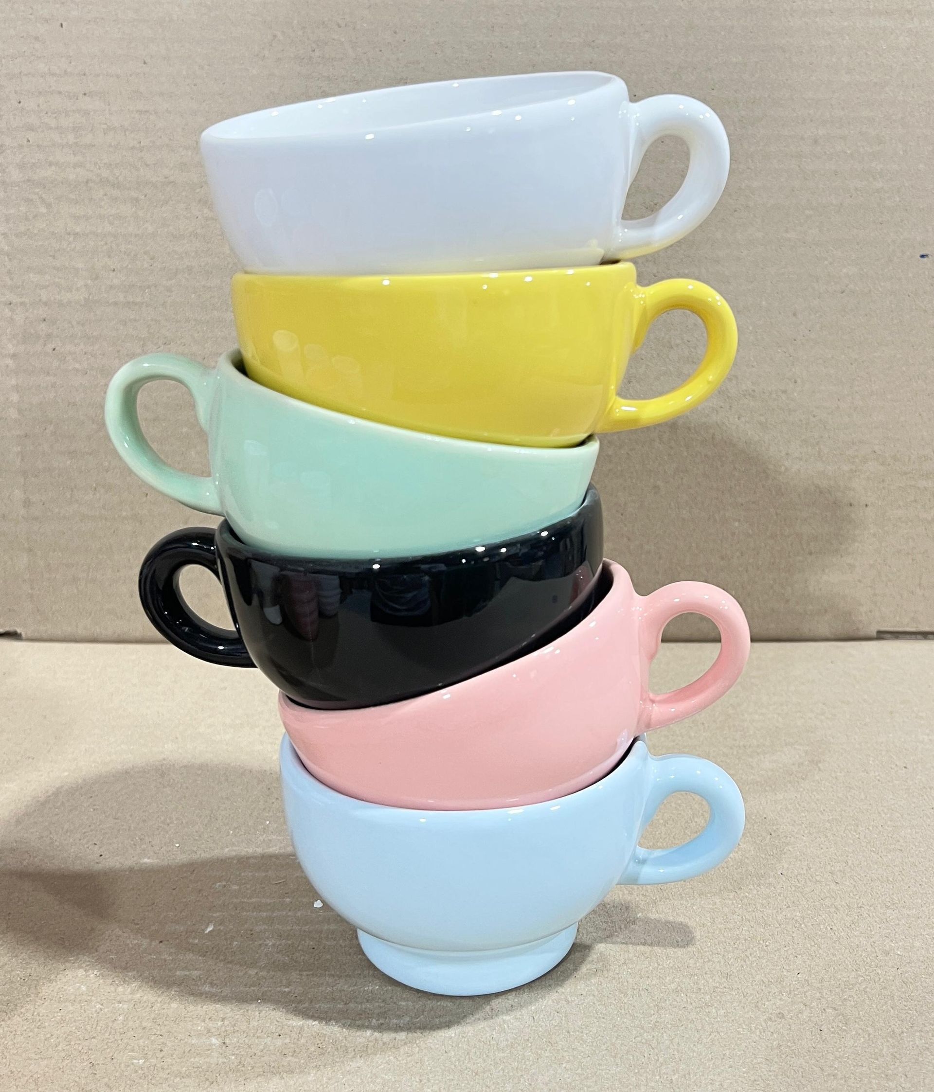 Pila de seis tazas de té de colores: blanco, amarillo, verde menta, negro, rosa y azul claro.