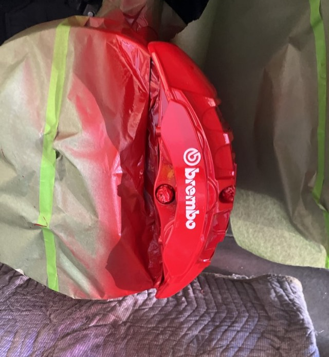 A red brembo brake caliper is wrapped in plastic