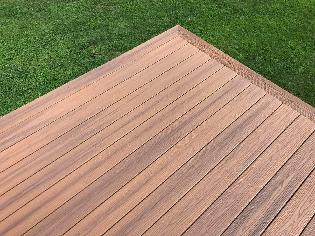 A high-angle view of a wooden deck corner made of brown planks surrounded by a green grass lawn.