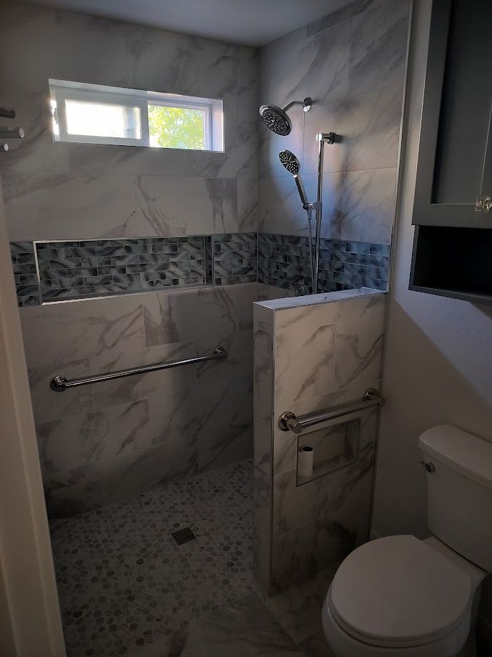 A bathroom features a walk-in shower with marble-look tile, a decorative blue mosaic inlay, and chrome grab bars.