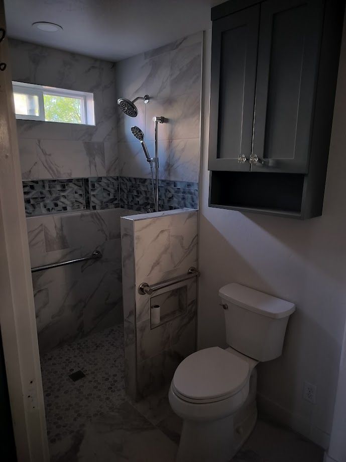 A bathroom featuring a shower with marble-look tile, grab bars, a rainfall showerhead, and an adjacent toilet.